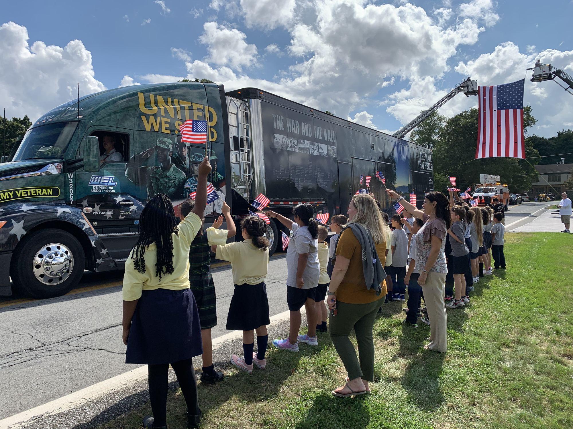 Schoolchildren wave American flags as The Wall That Heals truck passes