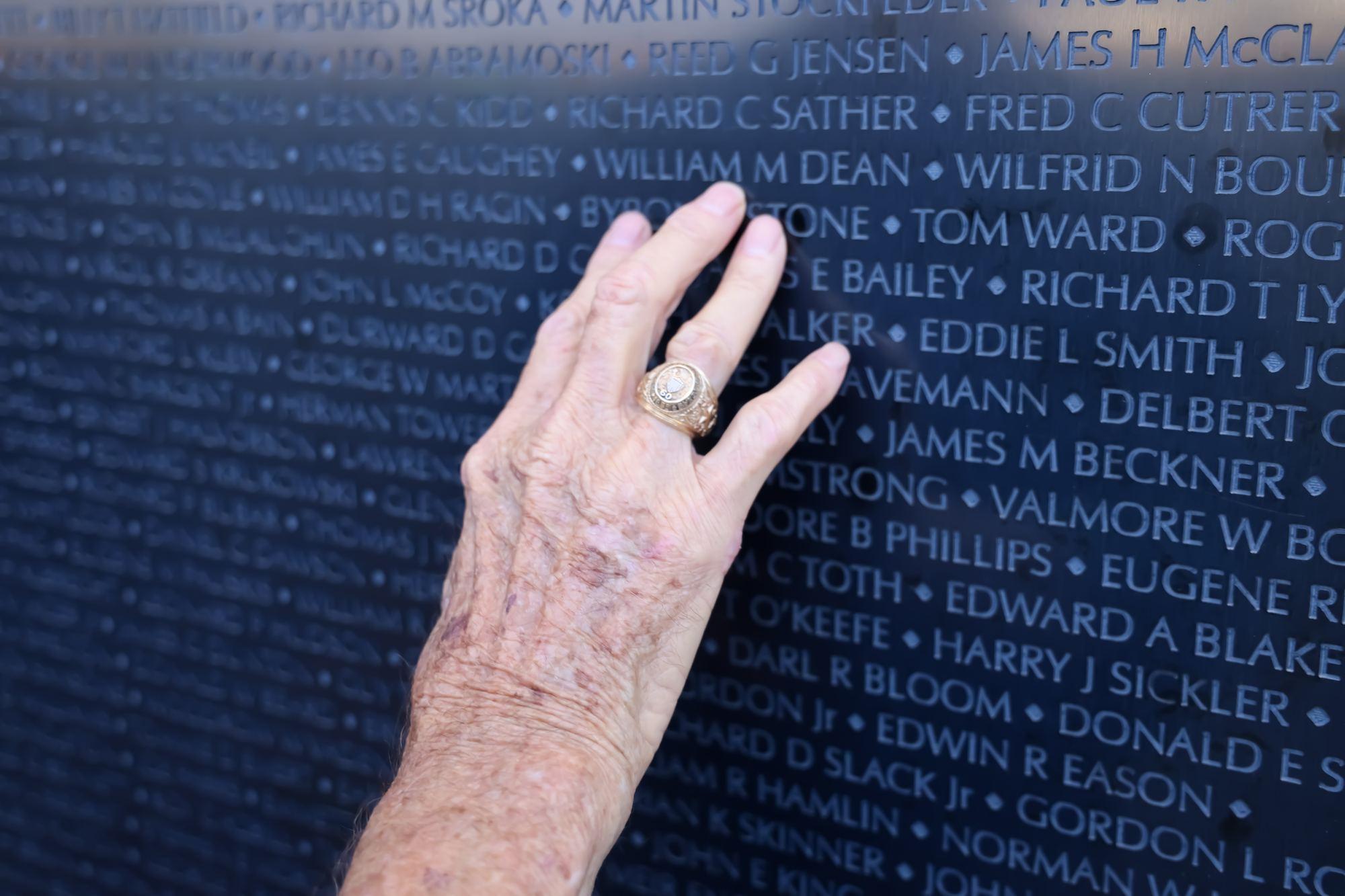 An elderly hand wearing a class ring rests against the engraved names