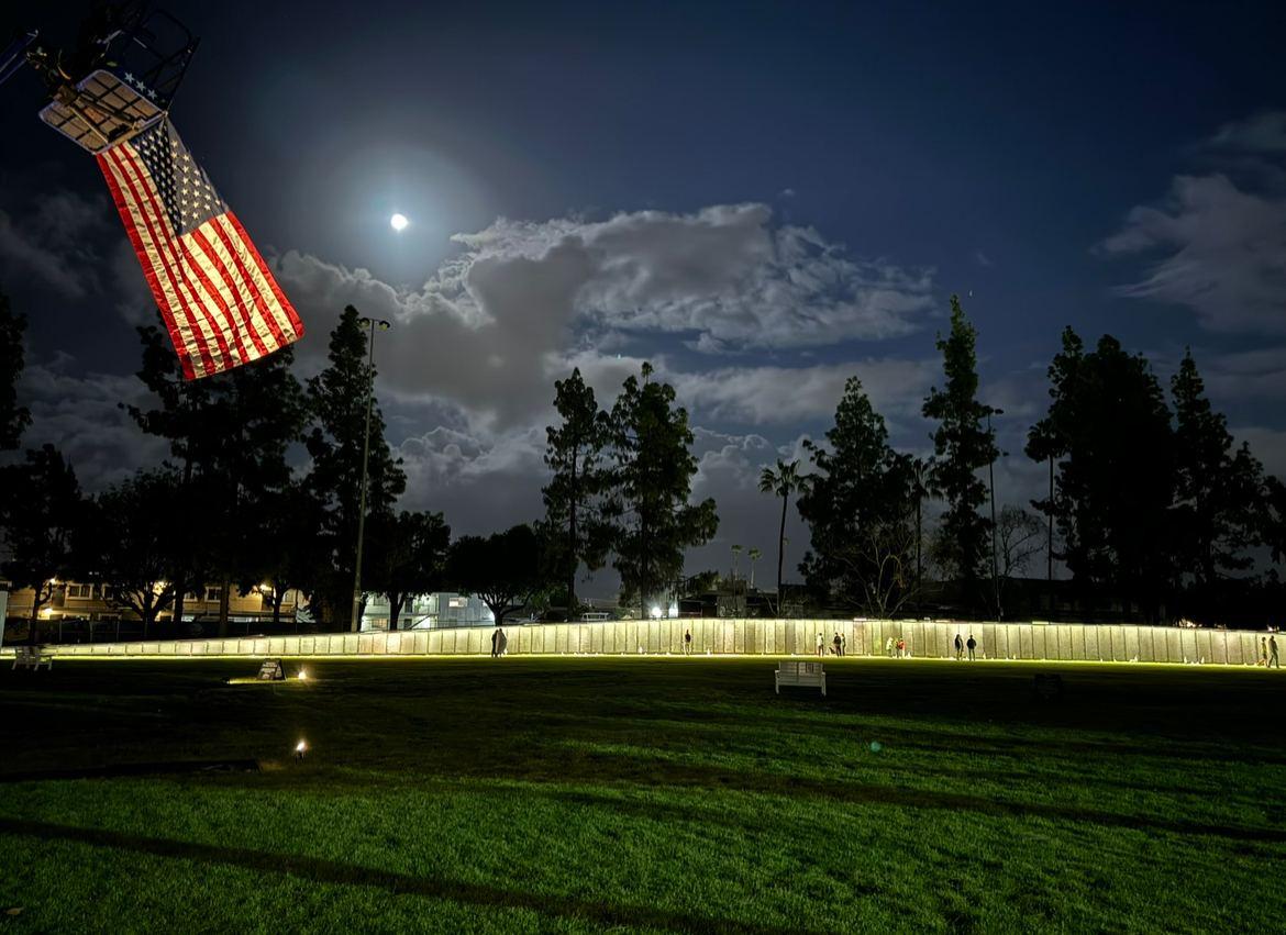 The Wall That Heals illuminated beneath a full moon, an American flag suspended above