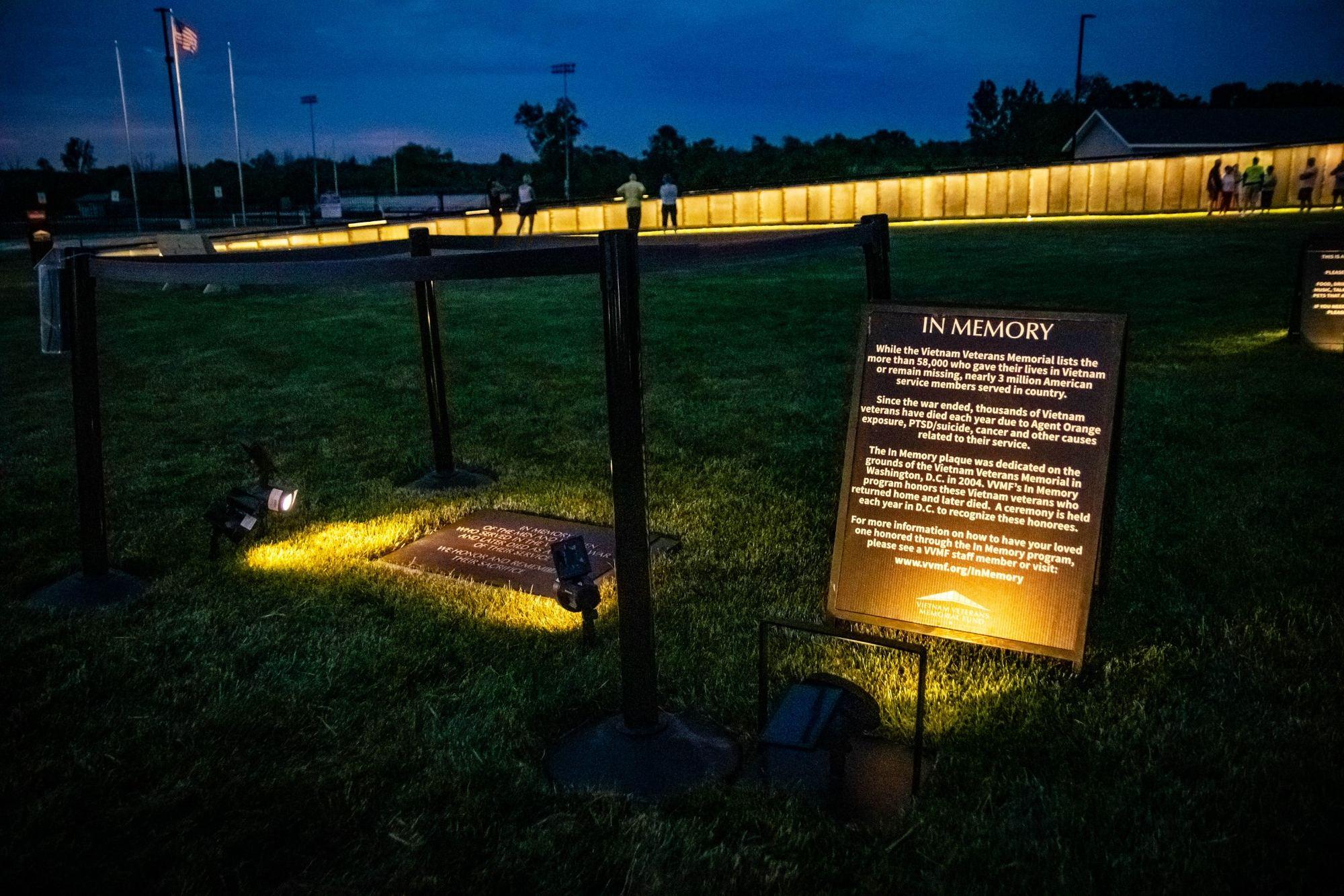 The In Memory plaque display illuminated at night beside The Wall