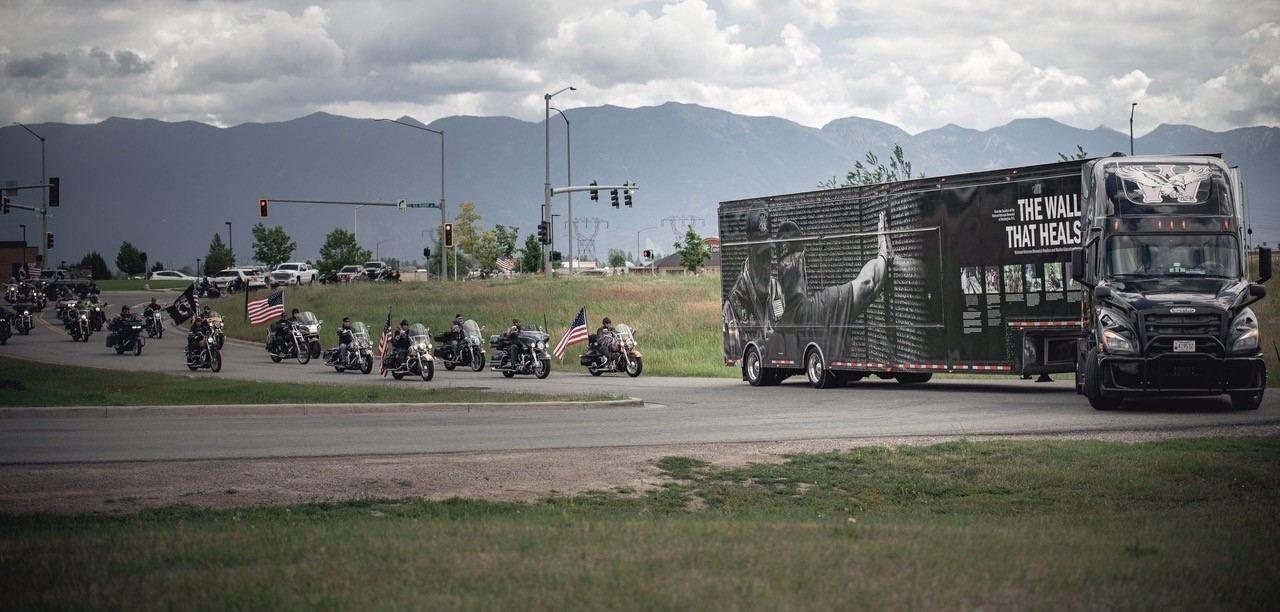 A long line of motorcycles escorts The Wall That Heals semi beneath mountain skies