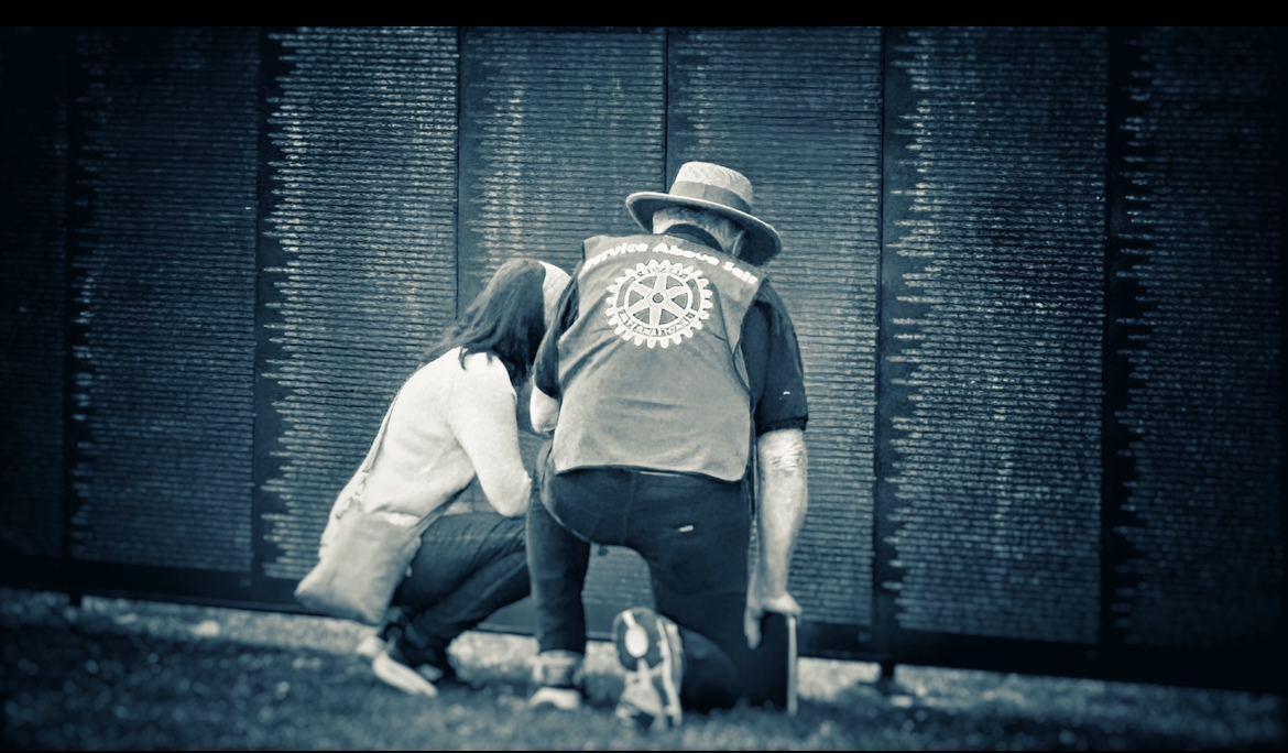 A volunteer kneels beside a visitor at The Wall